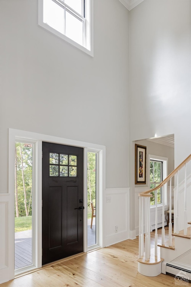 foyer with light hardwood / wood-style floors, crown molding, a high ceiling, and a baseboard radiator