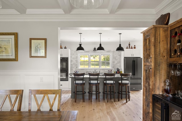 interior space with a kitchen bar, high end refrigerator, decorative light fixtures, light hardwood / wood-style floors, and white cabinetry