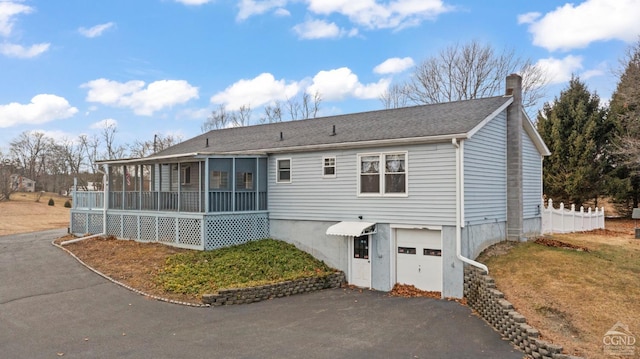 view of front of house with a garage, driveway, a chimney, and a sunroom