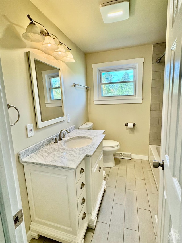 full bathroom with tiled shower / bath, vanity, toilet, and plenty of natural light