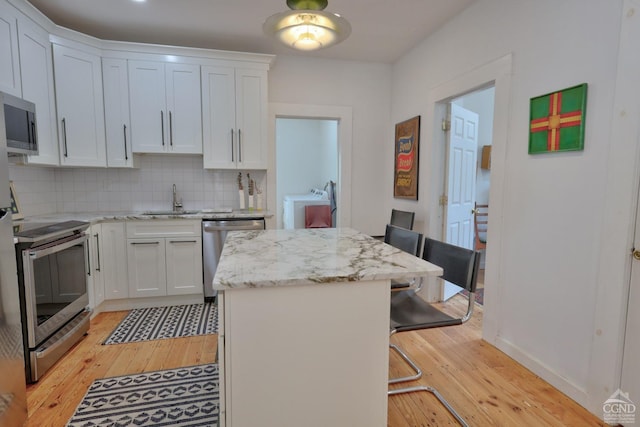 kitchen featuring white cabinets, light hardwood / wood-style floors, a kitchen bar, and stainless steel appliances