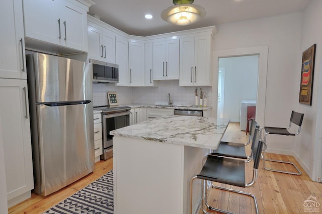 kitchen featuring light stone counters, white cabinets, stainless steel appliances, and light hardwood / wood-style floors