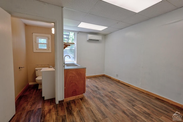 interior space featuring a drop ceiling, an AC wall unit, sink, and dark wood-type flooring