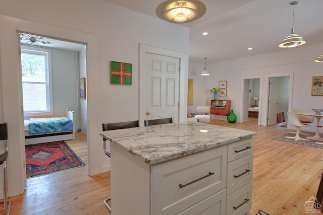 kitchen with white cabinets, light stone countertops, light hardwood / wood-style flooring, and hanging light fixtures