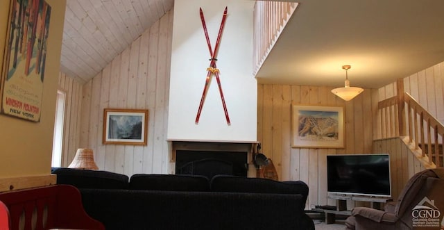 living area featuring lofted ceiling, a fireplace, wooden walls, and stairs