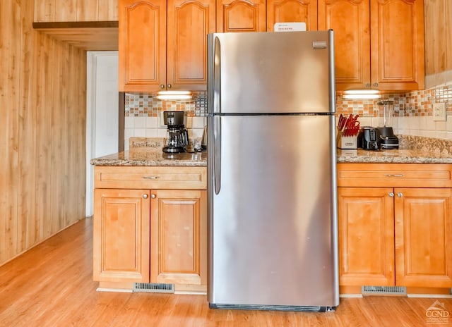 kitchen featuring tasteful backsplash, stainless steel fridge, light stone countertops, and light wood-type flooring