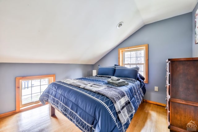 bedroom with vaulted ceiling, light wood-type flooring, and multiple windows