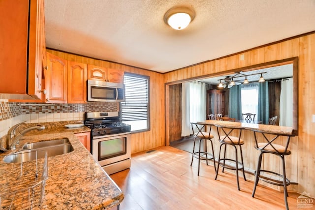 kitchen featuring a breakfast bar, sink, a textured ceiling, light stone counters, and stainless steel appliances