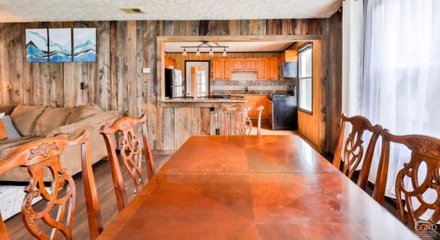 dining area featuring wood walls, light wood-type flooring, and track lighting