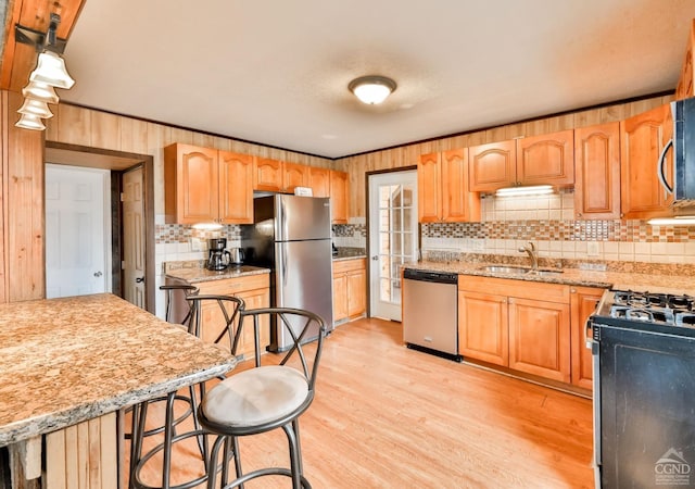 kitchen featuring light stone counters, a breakfast bar, stainless steel appliances, sink, and light hardwood / wood-style flooring