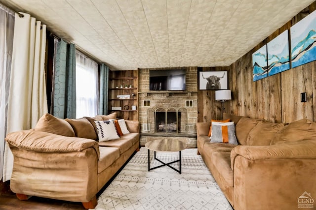 living room featuring built in shelves, a stone fireplace, and wooden walls