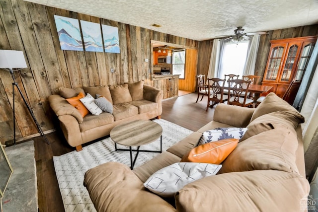 living room featuring hardwood / wood-style flooring, ceiling fan, and wood walls