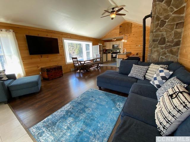 living room with hardwood / wood-style flooring, ceiling fan, a wood stove, and wooden walls