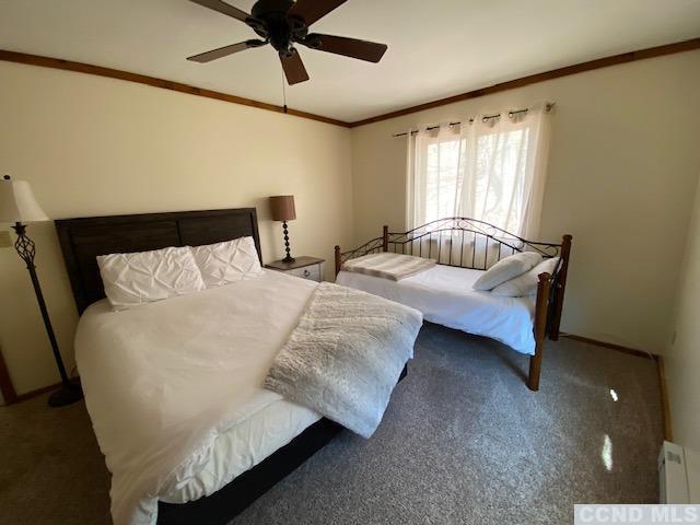 bedroom with carpet flooring, baseboard heating, ceiling fan, and crown molding