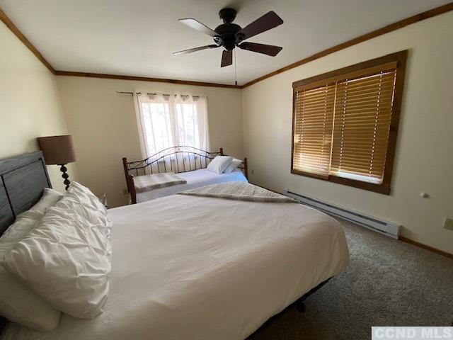 carpeted bedroom featuring ceiling fan, crown molding, and a baseboard radiator