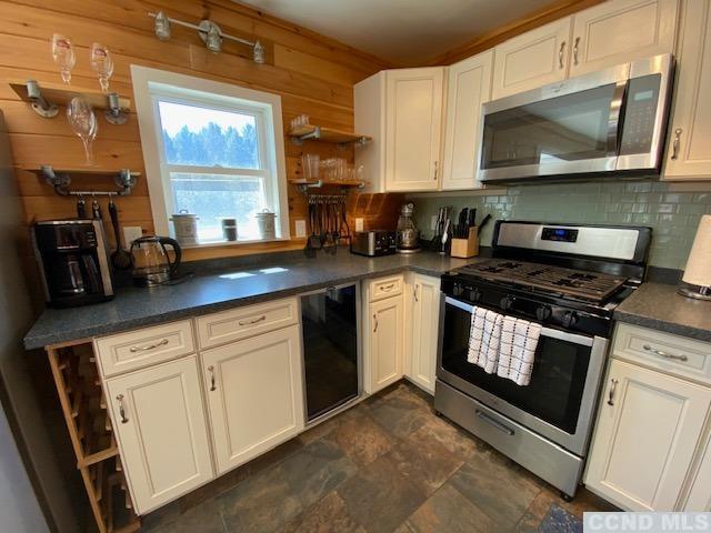 kitchen with tasteful backsplash, stainless steel appliances, white cabinetry, wine cooler, and wood walls