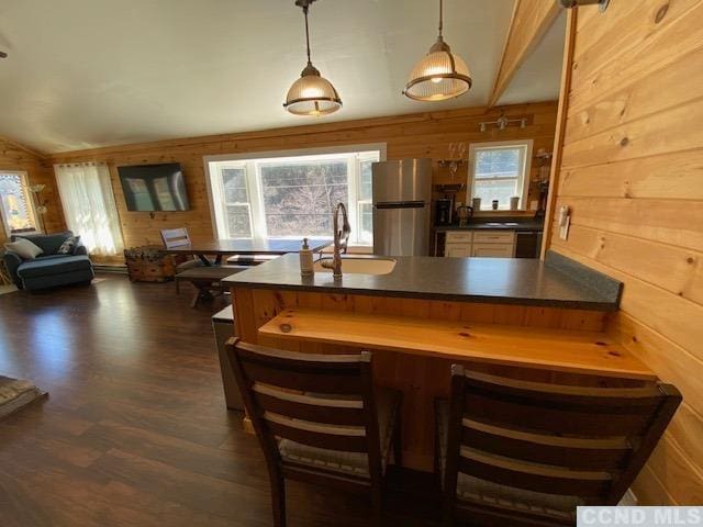 kitchen featuring sink, wooden walls, stainless steel fridge, decorative light fixtures, and dark hardwood / wood-style flooring