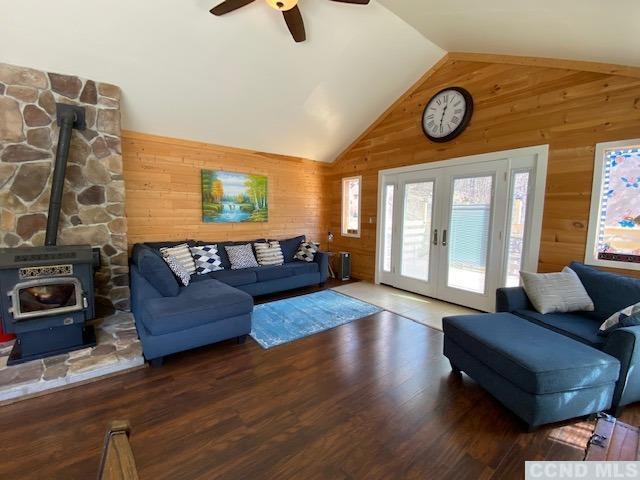 living room featuring french doors, dark hardwood / wood-style flooring, ceiling fan, wooden walls, and a wood stove