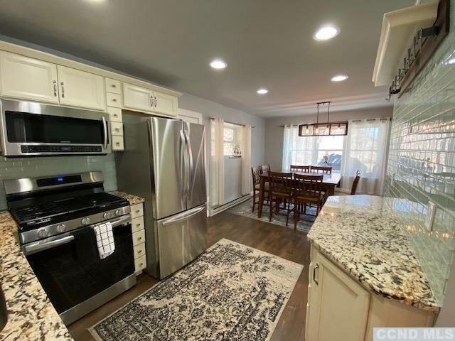 kitchen with a center island, dark wood-type flooring, hanging light fixtures, light stone counters, and stainless steel appliances