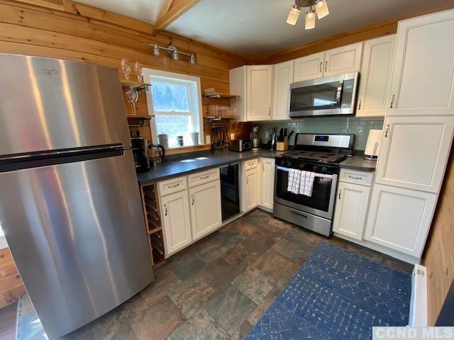 kitchen featuring wooden walls, appliances with stainless steel finishes, tasteful backsplash, white cabinetry, and beverage cooler