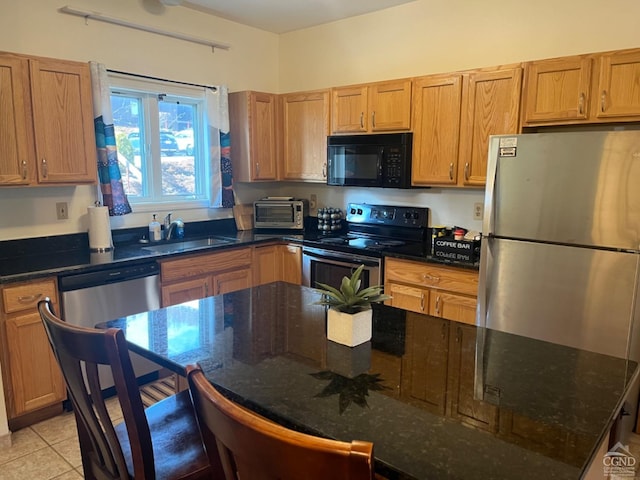 kitchen with a toaster, dark stone countertops, light tile patterned flooring, stainless steel appliances, and a sink