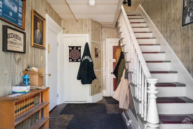 mudroom with dark tile patterned flooring, a drop ceiling, and wood walls