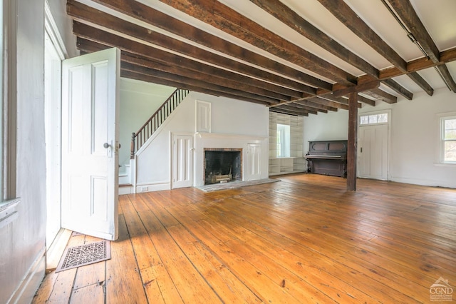 unfurnished living room with stairs, hardwood / wood-style flooring, a fireplace with raised hearth, beam ceiling, and visible vents