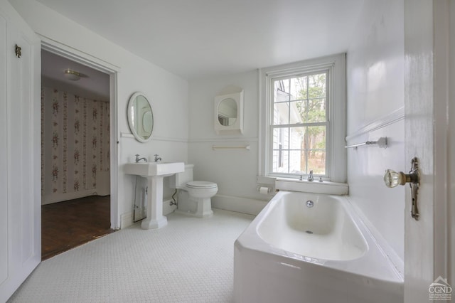 full bath featuring toilet, a bath, and baseboards