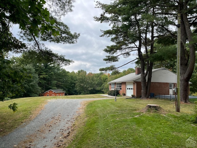 view of front of house with a front yard, a garage, a chimney, brick siding, and gravel driveway