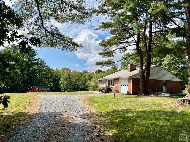 view of front of property with an attached garage, a chimney, driveway, and a front lawn