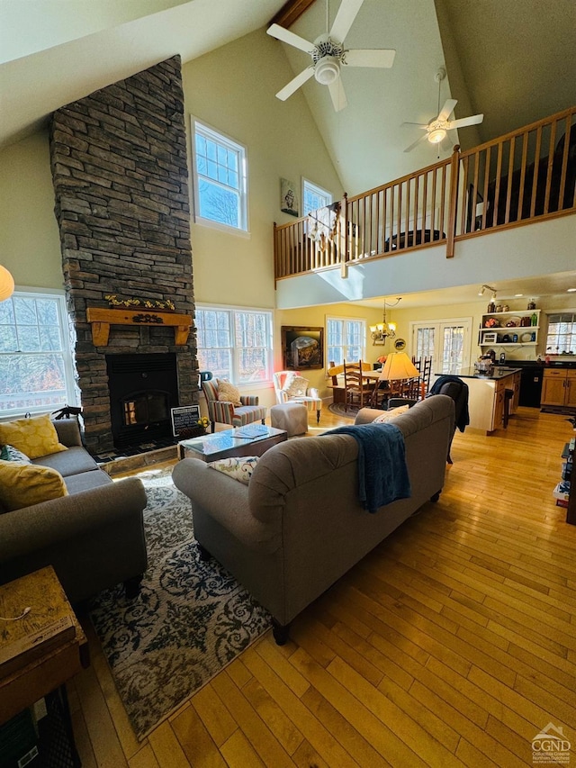 living room with a fireplace, high vaulted ceiling, light hardwood / wood-style floors, and ceiling fan with notable chandelier