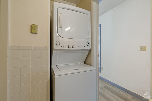 washroom featuring tile walls, light hardwood / wood-style floors, and stacked washer / dryer