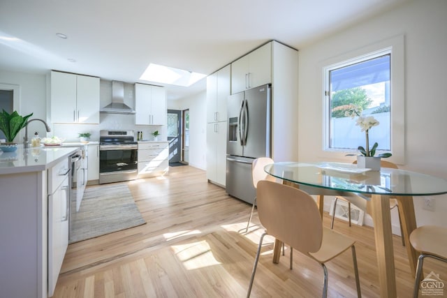 kitchen featuring decorative backsplash, wall chimney exhaust hood, stainless steel appliances, light hardwood / wood-style flooring, and white cabinetry