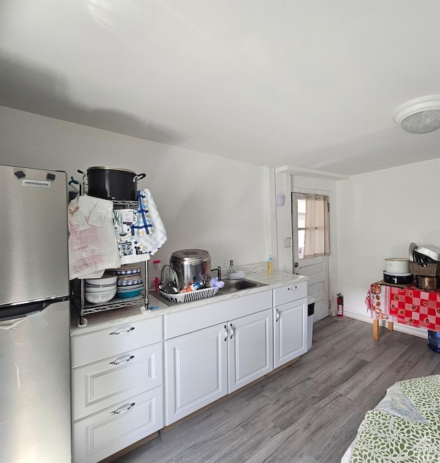 kitchen with light wood-type flooring, light countertops, white cabinets, baseboards, and freestanding refrigerator