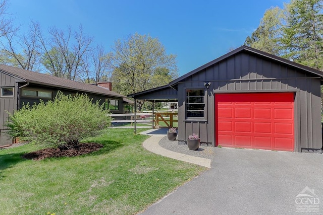 view of side of home with aphalt driveway, fence, board and batten siding, a yard, and a detached garage