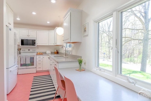 kitchen with white cabinets, a sink, white appliances, light countertops, and ornamental molding