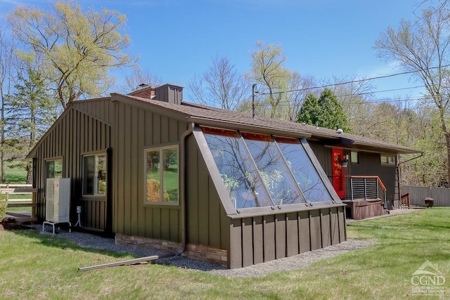 rear view of house featuring board and batten siding, a yard, fence, and a chimney