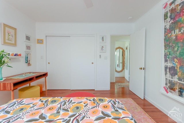 bedroom featuring a closet, crown molding, wood finished floors, baseboards, and a ceiling fan