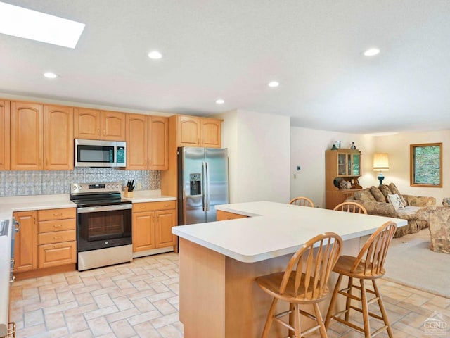 kitchen featuring a center island, a skylight, appliances with stainless steel finishes, tasteful backsplash, and a kitchen bar