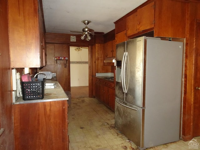 kitchen featuring a ceiling fan, brown cabinets, light floors, stainless steel refrigerator with ice dispenser, and under cabinet range hood