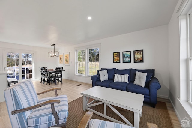 living room featuring light wood-type flooring, plenty of natural light, and a notable chandelier