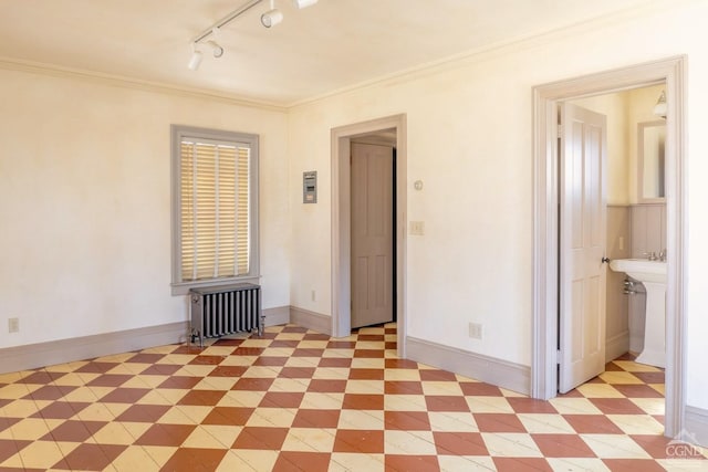 spare room featuring radiator, track lighting, light floors, baseboards, and ornamental molding