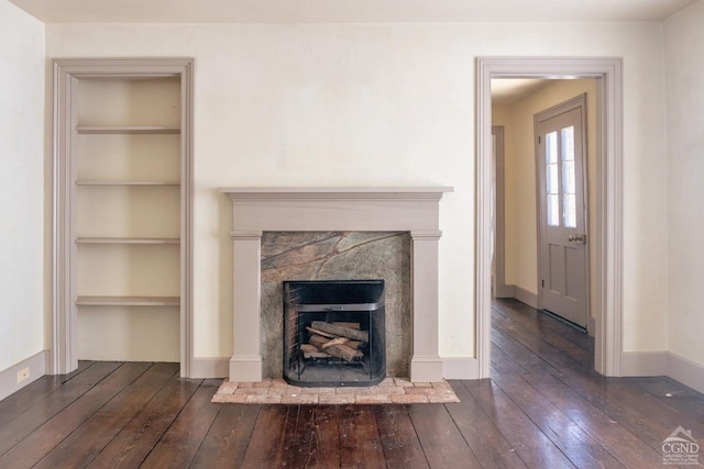 unfurnished living room with built in features, a fireplace, baseboards, and wood-type flooring