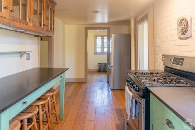 kitchen with radiator heating unit, light wood finished floors, glass insert cabinets, green cabinets, and appliances with stainless steel finishes