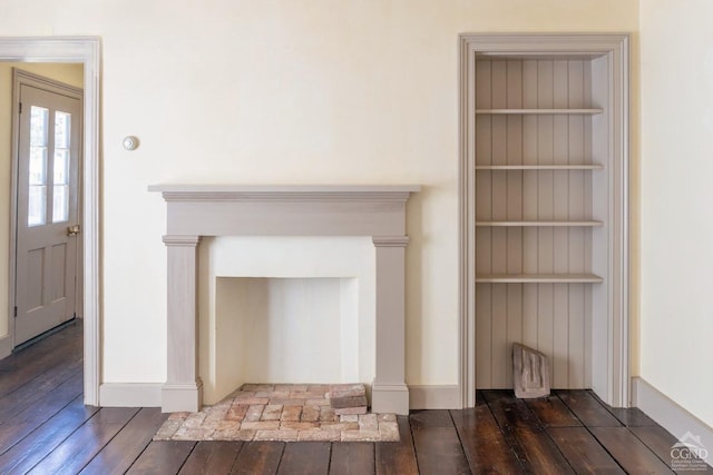 unfurnished living room featuring baseboards, wood-type flooring, and built in features