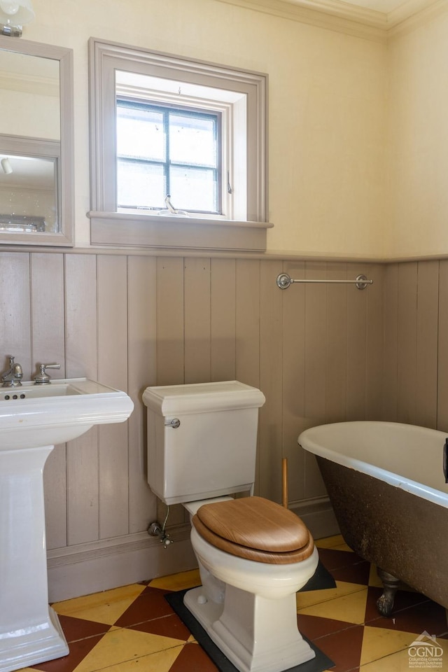 bathroom with a freestanding bath, toilet, crown molding, and a wainscoted wall