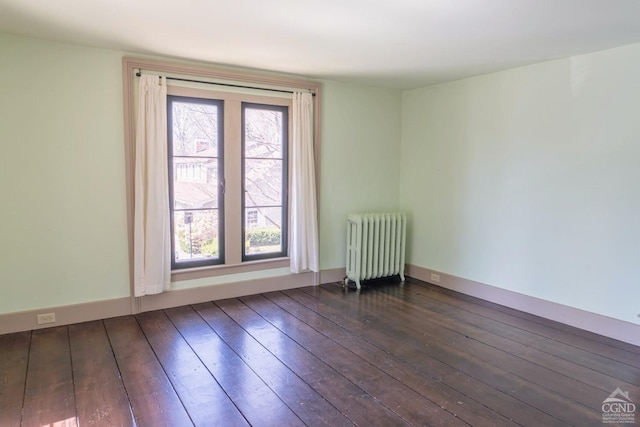 spare room featuring baseboards, dark wood-style flooring, and radiator heating unit