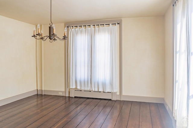 empty room with baseboards, a notable chandelier, baseboard heating, and dark wood finished floors