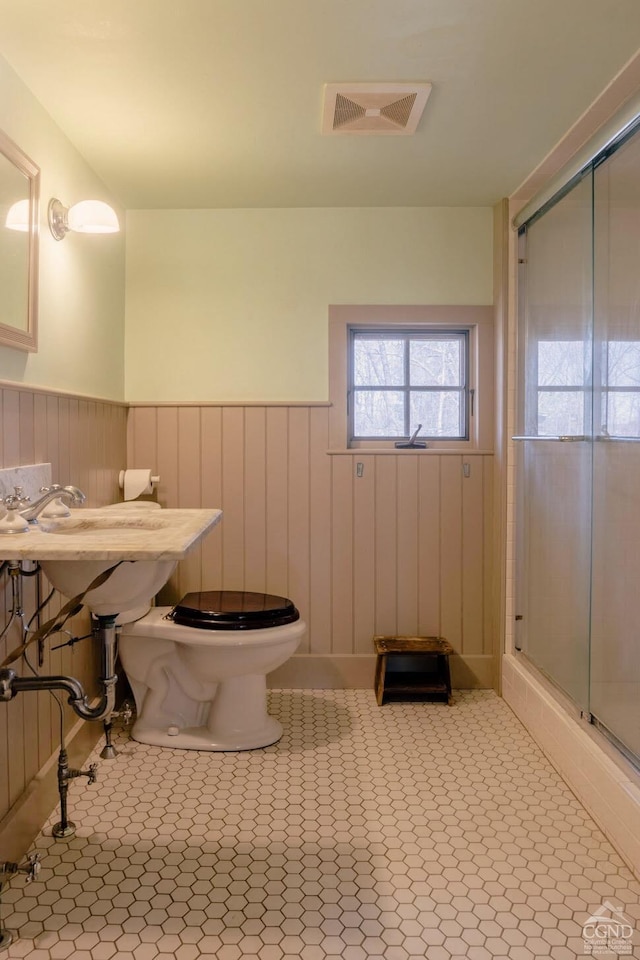 full bath featuring a stall shower, toilet, wainscoting, visible vents, and tile patterned flooring