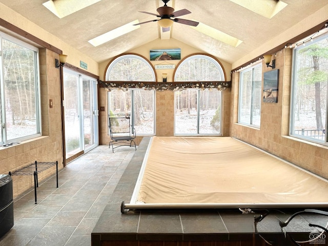 unfurnished sunroom with ceiling fan, vaulted ceiling with skylight, and plenty of natural light